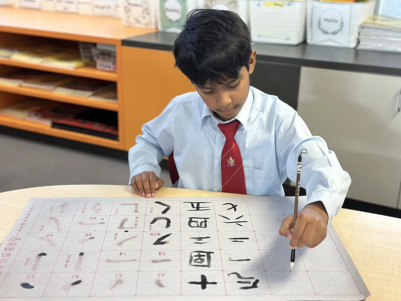 Middle primary school aged student from Junior School using traditional brushes to paint Chinese characters on a grid during Overnewton’s 2025 Languages and Culture Week.