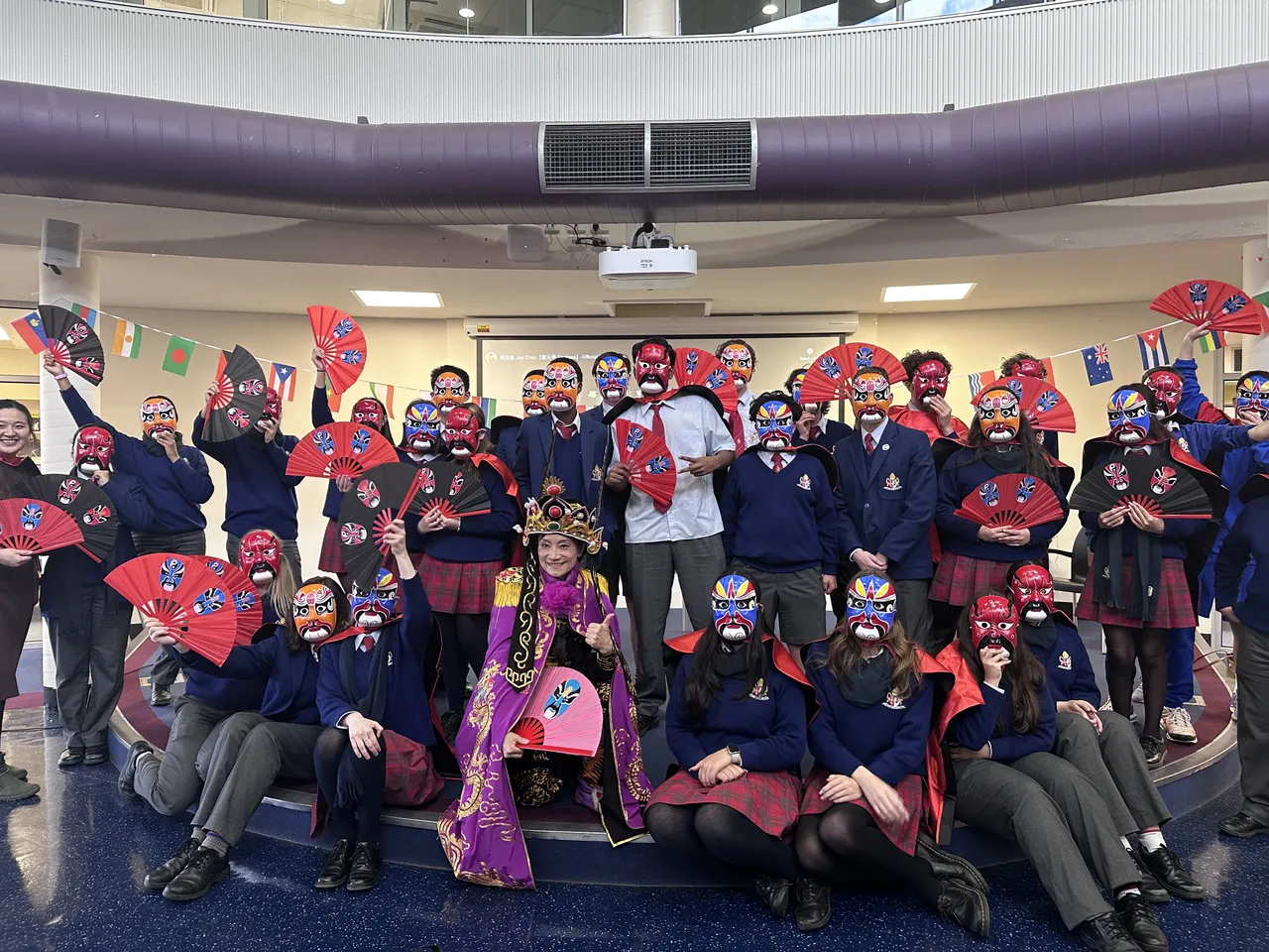 A large group of upper secondary school-aged students holding traditional red fans surround professional face-changing Sichual Opera artist during Overnewton's 2025 Languages and Culture Week.