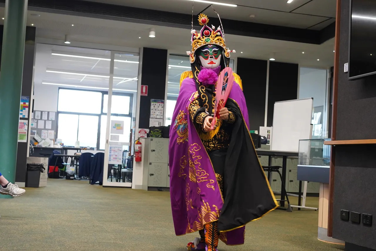 A professional face-changing Sichuan Opera artist in traditional dress performing extravagantly with a large fan for Middle School students at Yirramboi Campus Overnewton's 2025 Languages and Culture Week.