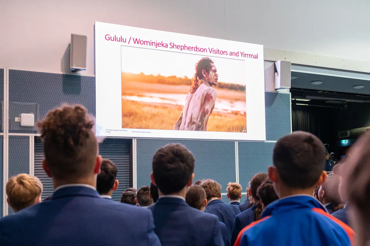 Middle and upper secondary school students from Overnewton Anglican Community College Middle School and Senior School looking up at screen featuring a welcome message in both English and local Wurundjeri language to open the 2025 Yirramboi Campus Reconciliation Assembly.
