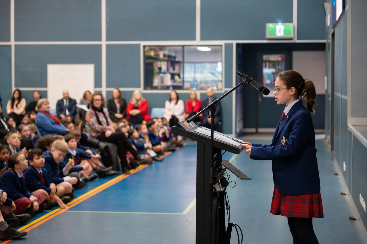 A middle secondary school-aged student leader stands at a lectern to address her fellow students, staff and guests as part of the Overnewton Anglican Community College 2025 Yirramboi Campus Reconciliation Week Assembly.