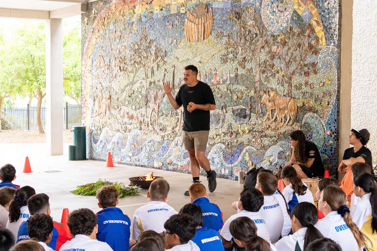 Thane, proud member of the Wurundjeri people of the Kulin Nation, standing beside a lit fire pit and sharing stories and teaching tradition with Year 5 students as part of an annual Smoking Ceremony for Year 5 students new to the Yirramboi Campus.