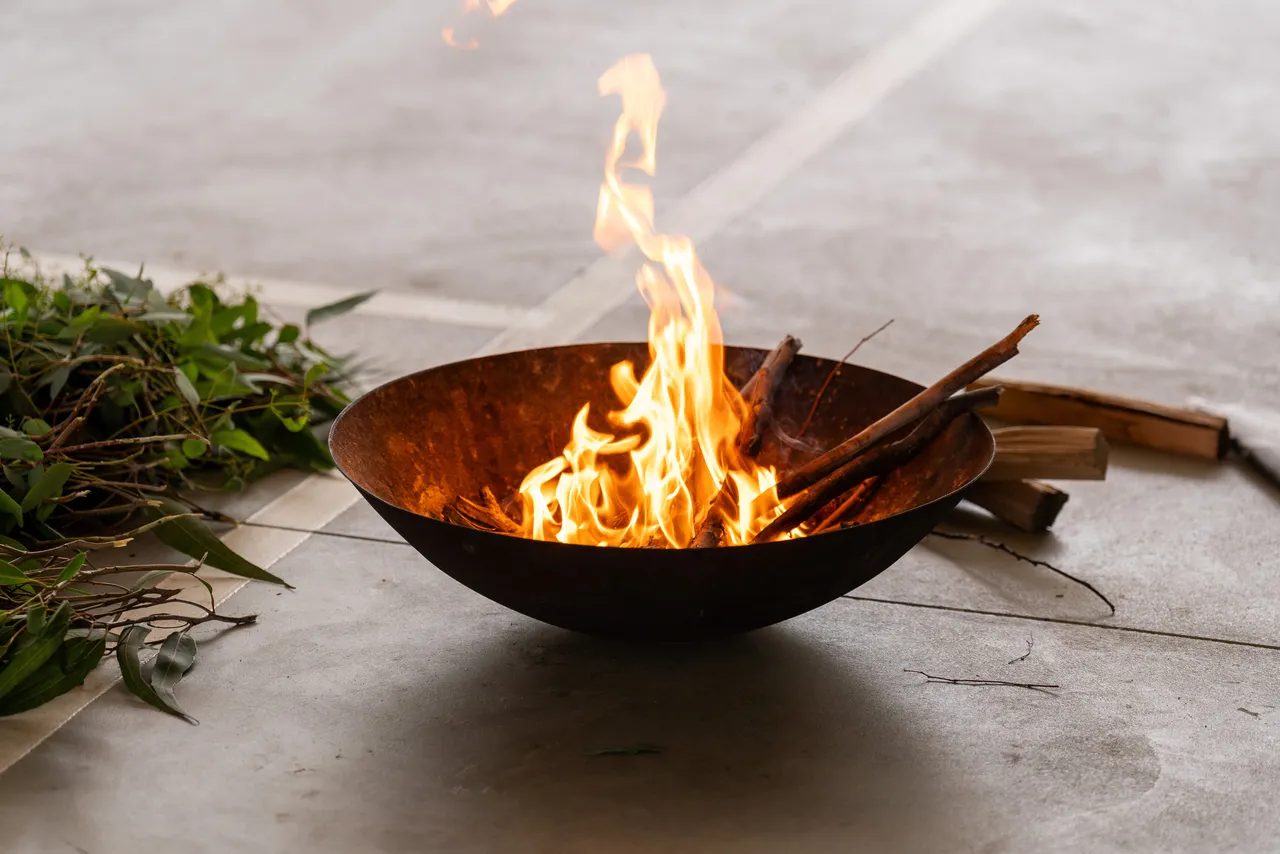 Close up of a lit fire pit beside a large eucalyptus branch during a Smoking Ceremony for Year 5 students new to the Yirramboi Campus.