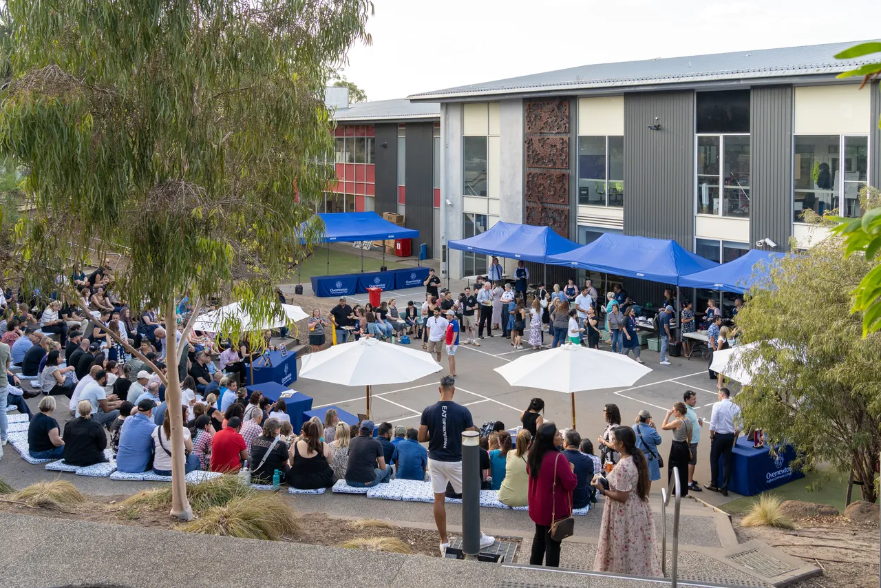 A large group of community members connecting and relaxing during a hot summer evening, attending the inaugural Yirramboi Parent Information Evening held in the Middle School Outdoor Amphitheatre.