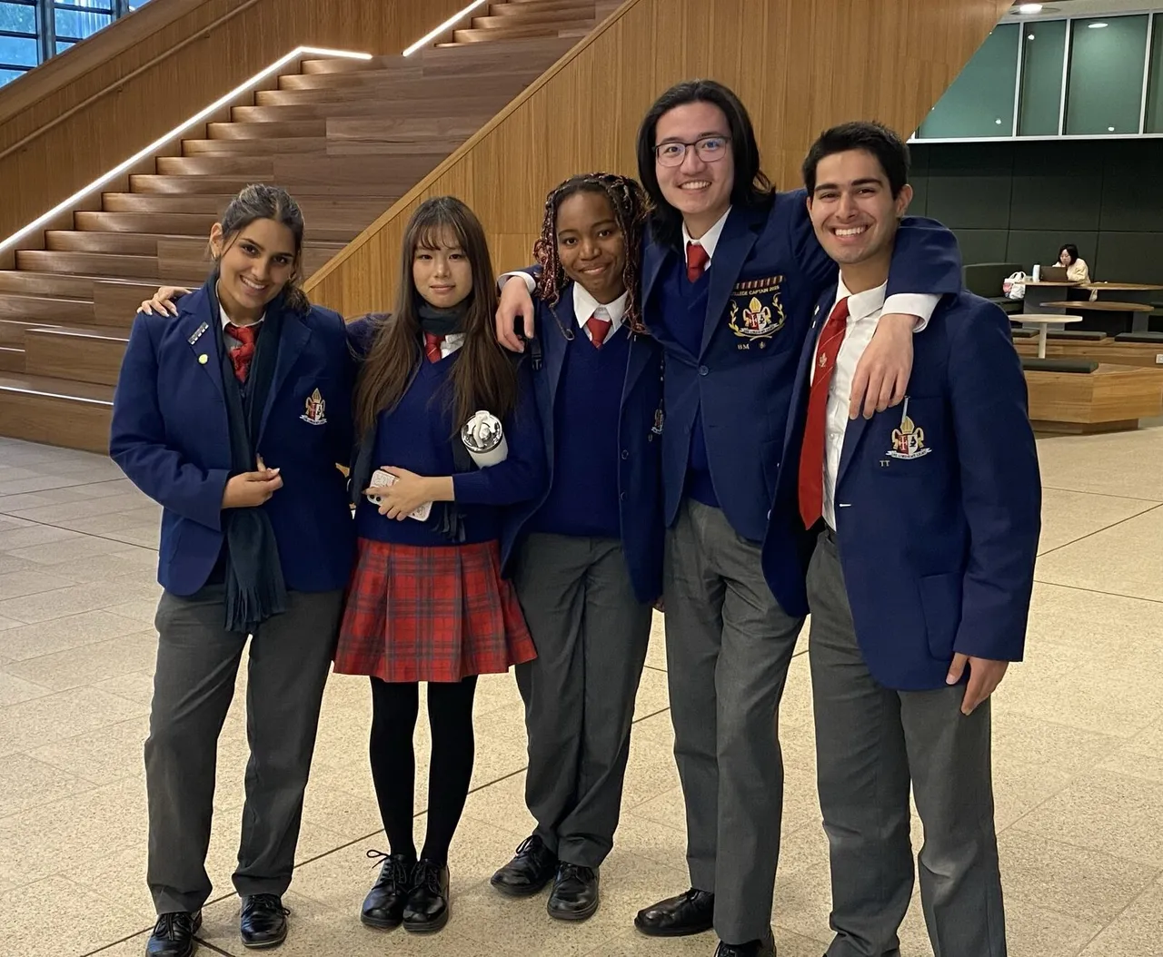 Group of upper secondary students standing together in a group shot in a foyer at Monash University.  The students are part of the Overnewton Year 12 Debating team who competed at the Monash Asian Studies Debating Competition.