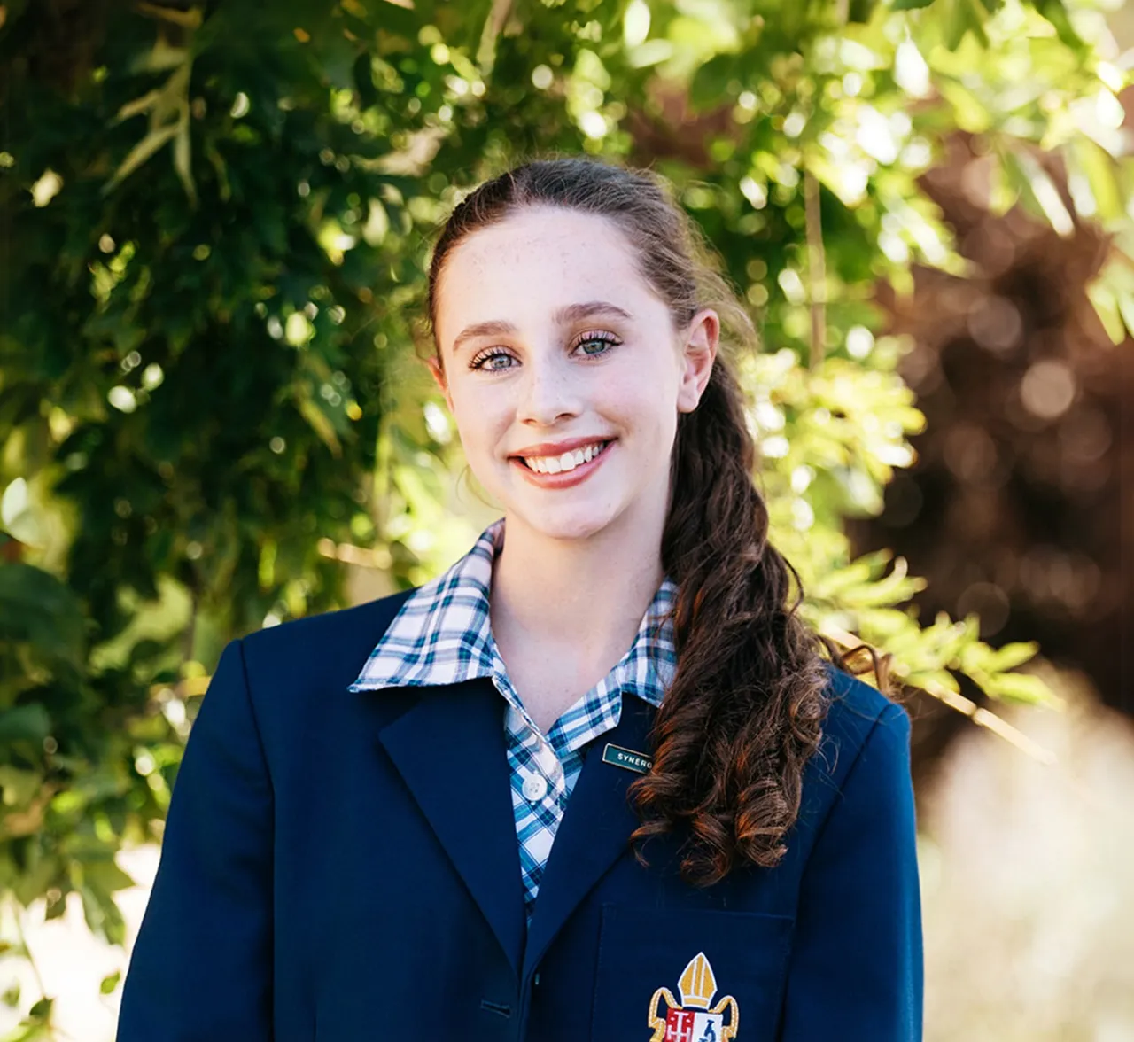 Upper high school aged Senior School student looking to camera with lush trees in the background