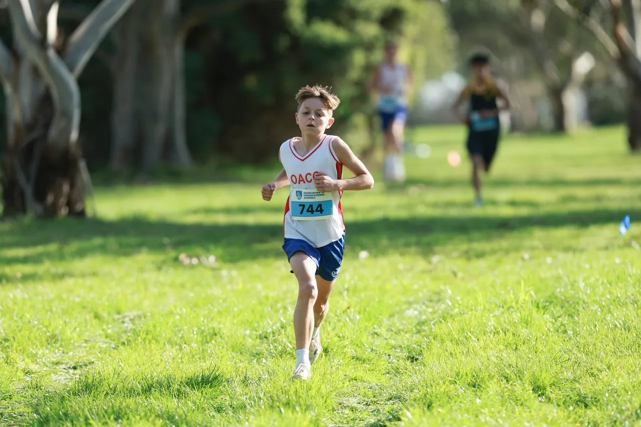 Middle secondary school aged student running toward the camera in a lush green park, representing Overnewton at the Association of Co-Educational Schools Cross Country Competition as part of the Activate Co Curricular program.