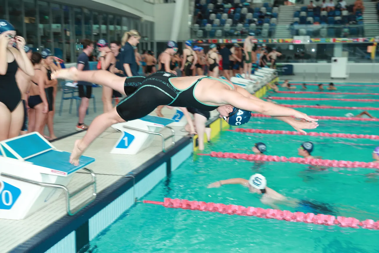 Upper secondary school aged student diving from a starting block into an indoor pool during the interschool Swimming competition for the Association of Co-Educational Schools, as part of Overnewton’s Activate Co Curricular program.
