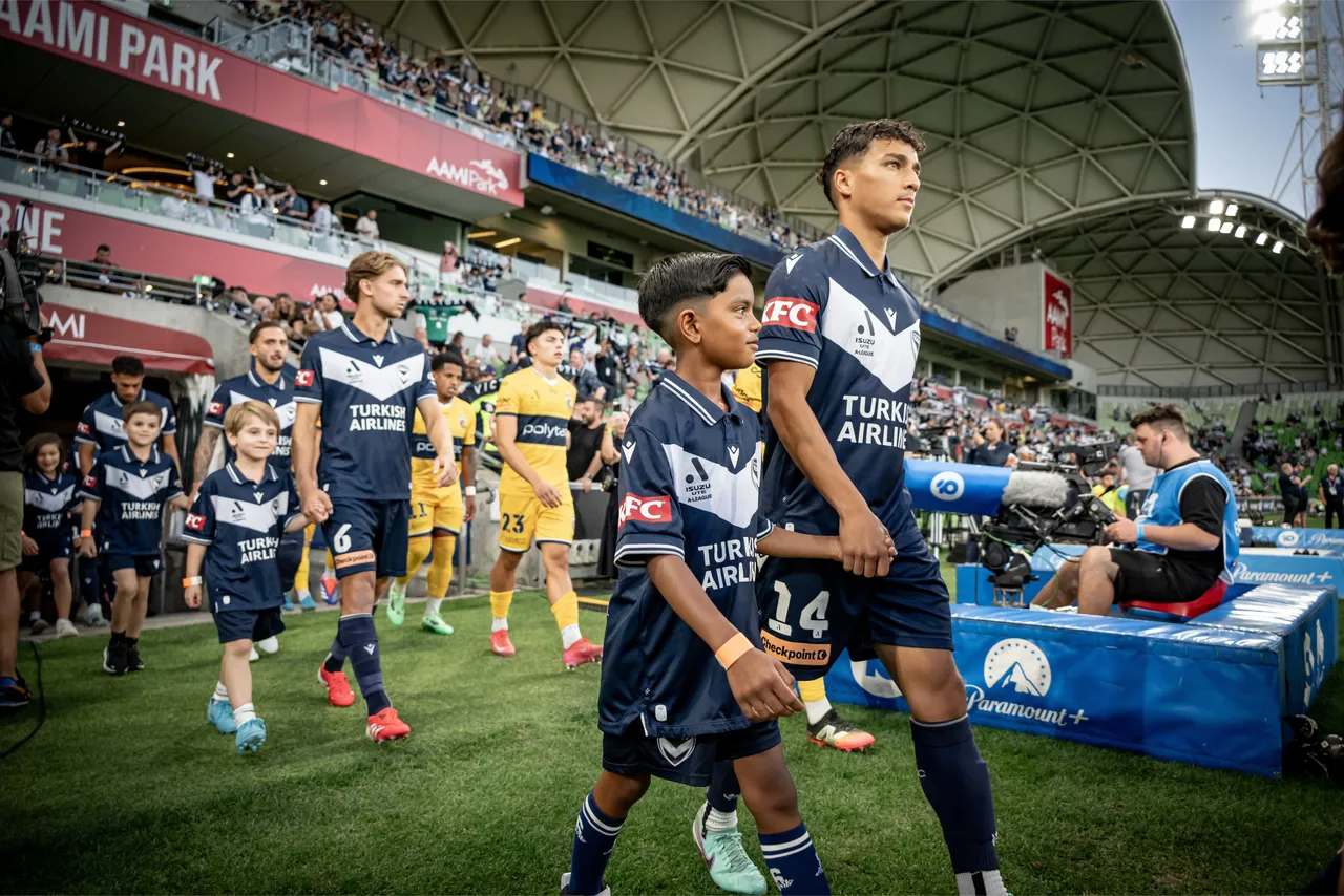 Overnewton students walking hand in hand with Melbourne Victory players as part of an exclusive match day experience at a professional game.