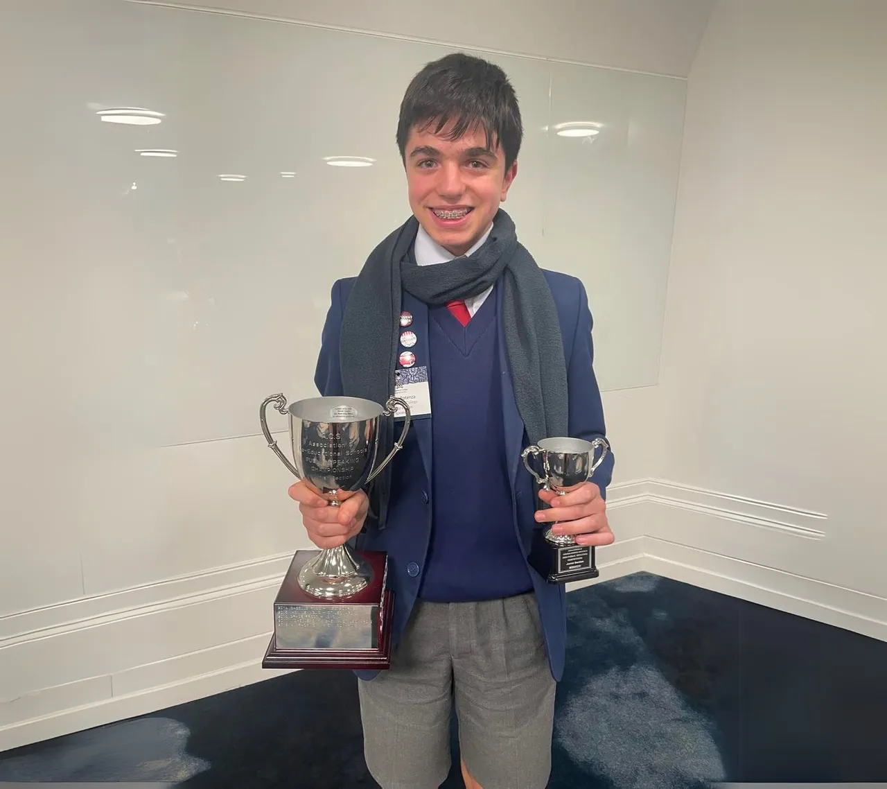 Proud upper secondary school aged student holding two winner’s trophies after placing first in the Junior Division of the Association of Co-Educational Schools Public Speaking Competition, as part of Overnewton's Be Heard Co Curricular program.