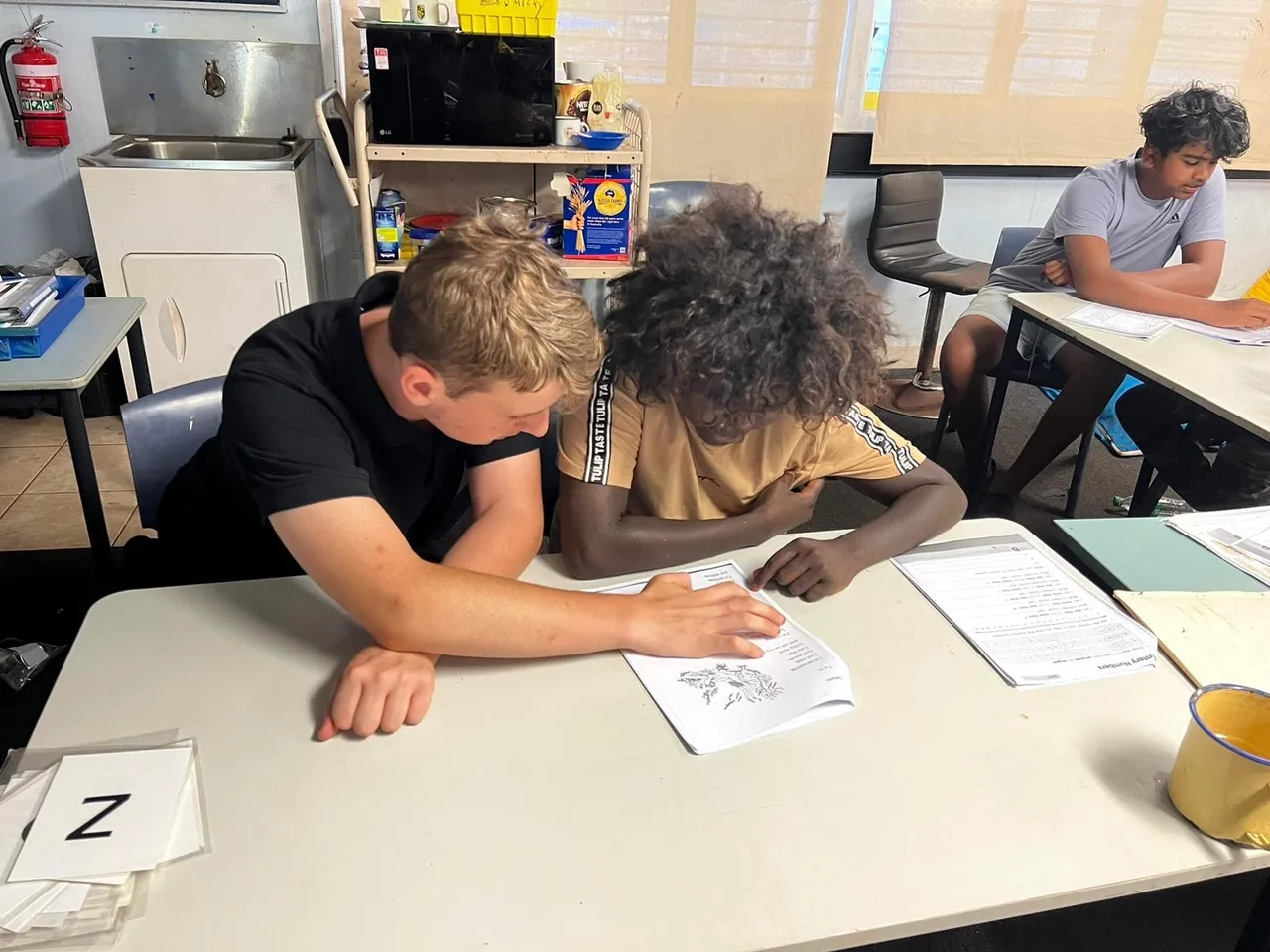 An upper secondary school aged student from Overnewton collaborating at a desk with a local Shepherdson College student, working together on a problem-solving activity.