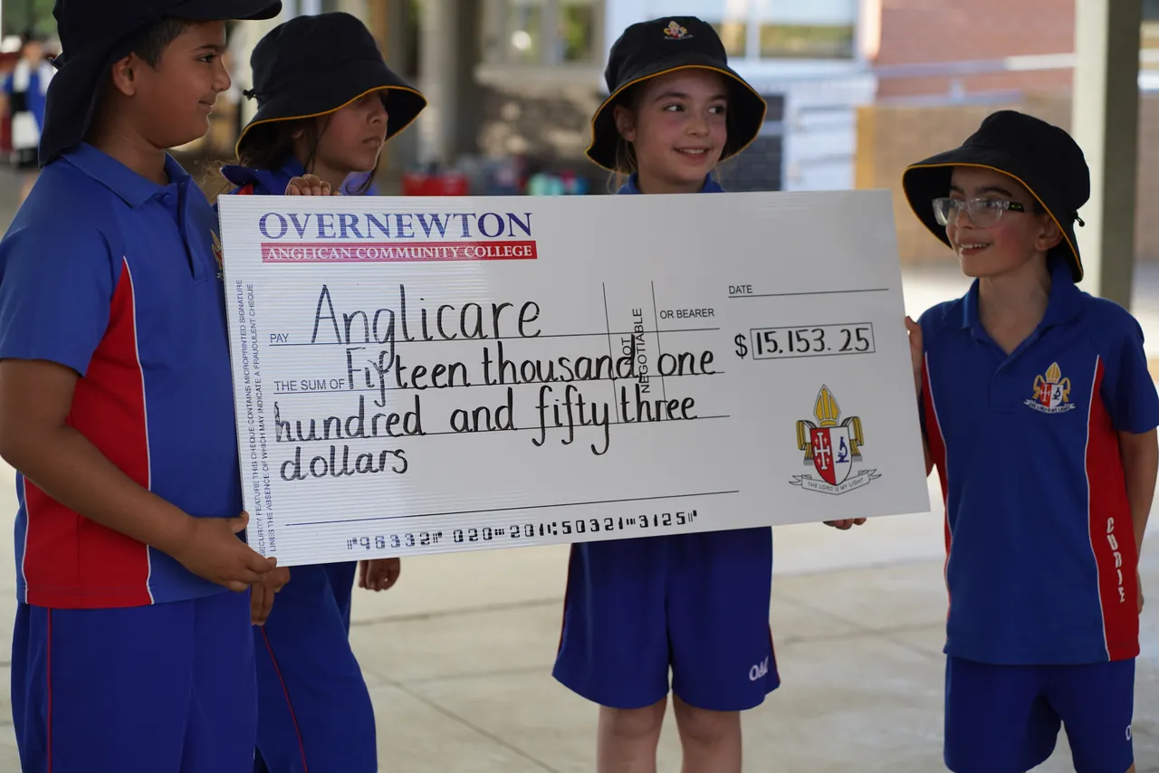 Four primary school aged students holding a large donation cheque for Anglicare Australia, representing Overnewton’s community giving efforts.