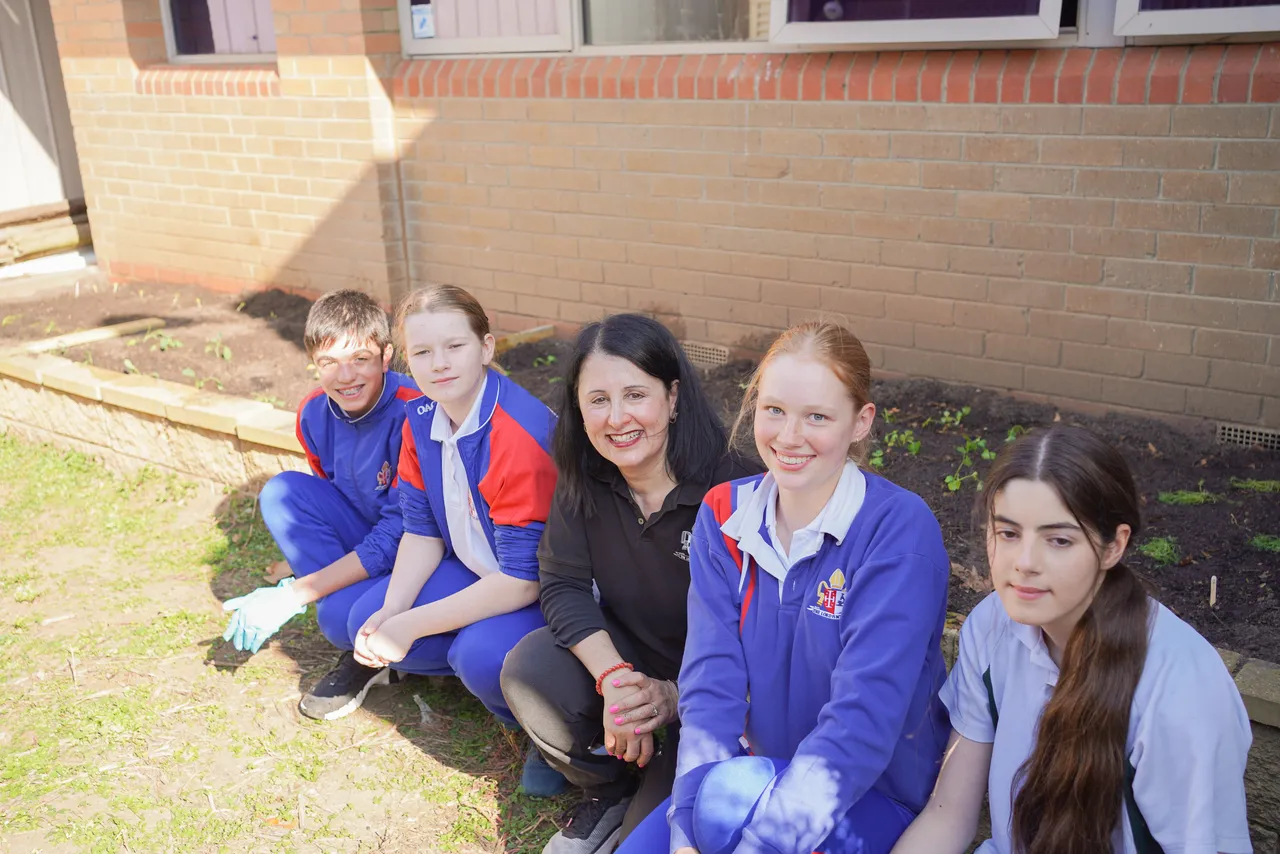 Lower high school aged students posing in a garden bed, planting vegetables as part of Overnewton’s sustainability program.