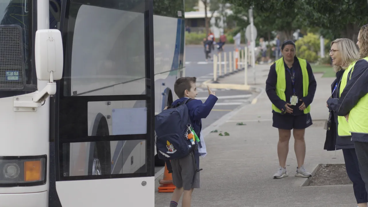 Lower primary school aged boy waving to staff on yard duty as he gets off the bus in the morning at Canowindra Campus.