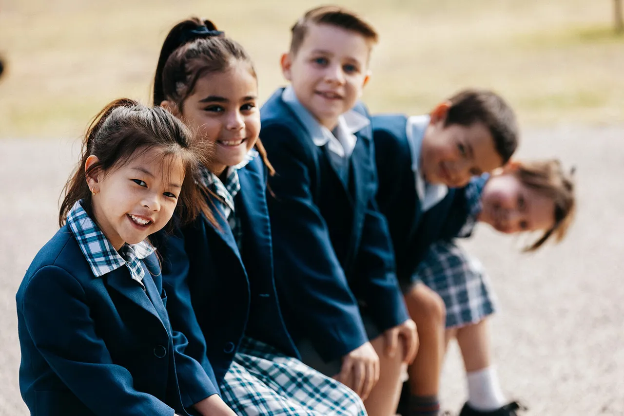 Five lower primary school aged students sitting together on a bench, smiling at Canowindra Campus