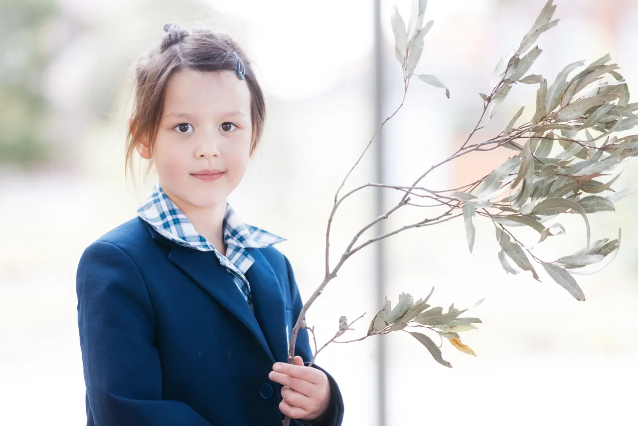 Lower primary school aged student looking at the camera, playing and holding a tree branch/twig in her hand.