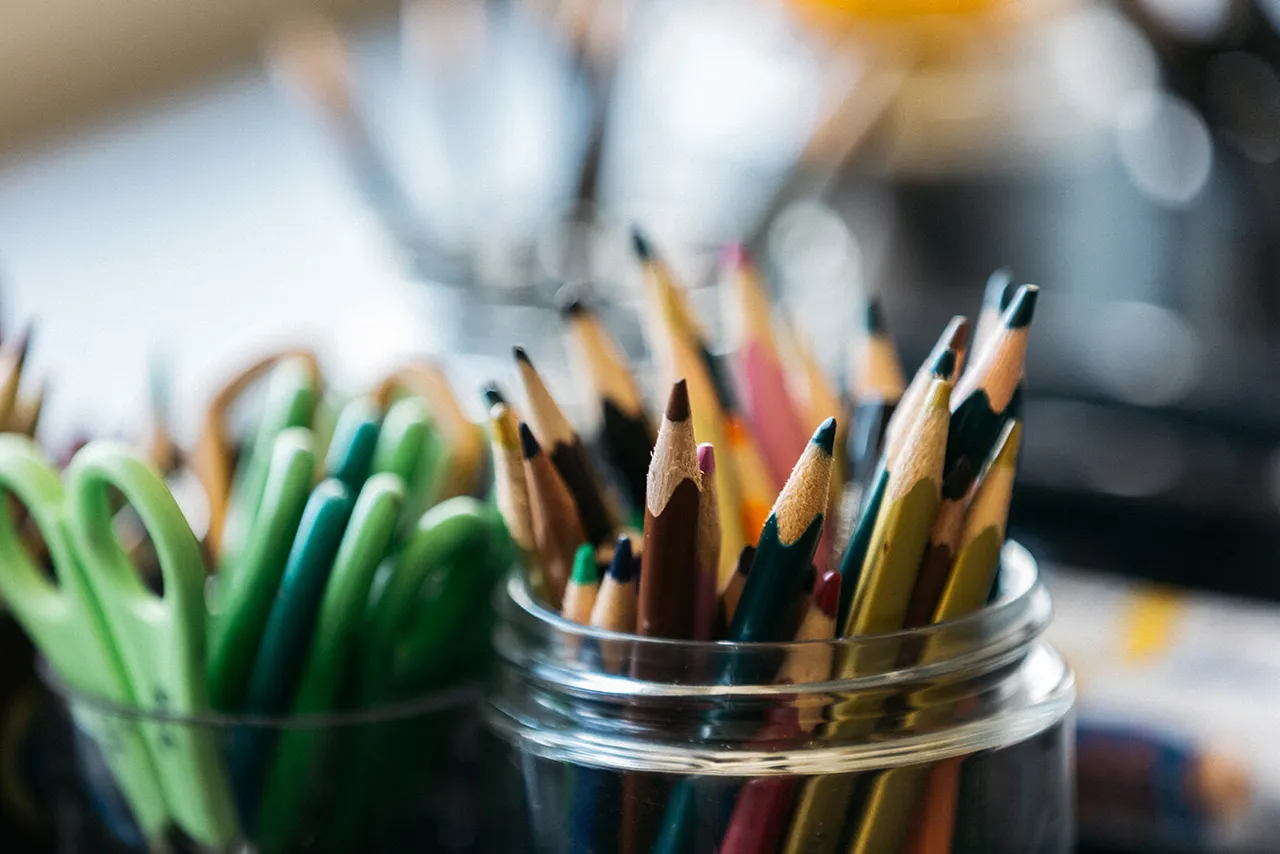 Artistic shot of a glass jar filled with coloured pencils and scissors, ready for creative work.