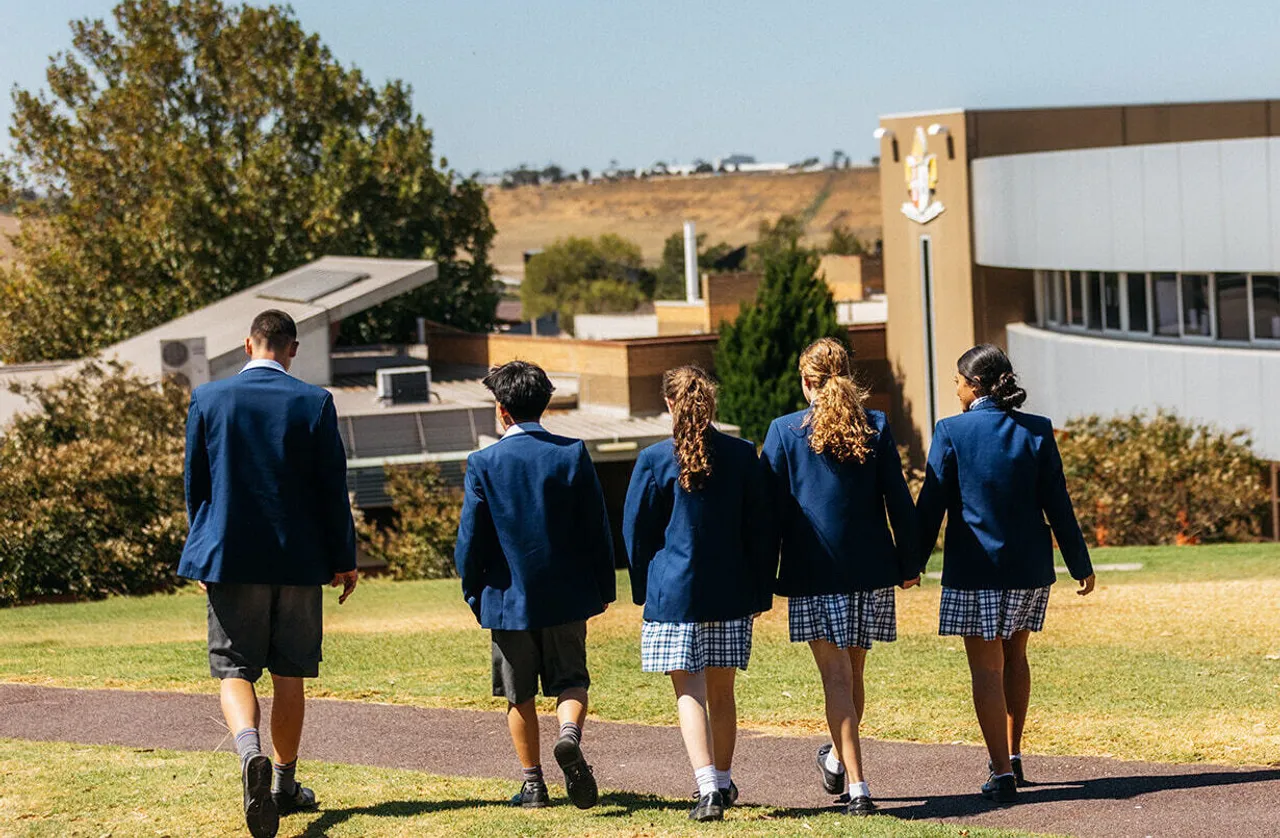 Five upper high school aged students walking through landscaped grounds at Yirramboi Campus, with the Senior School building in the background.