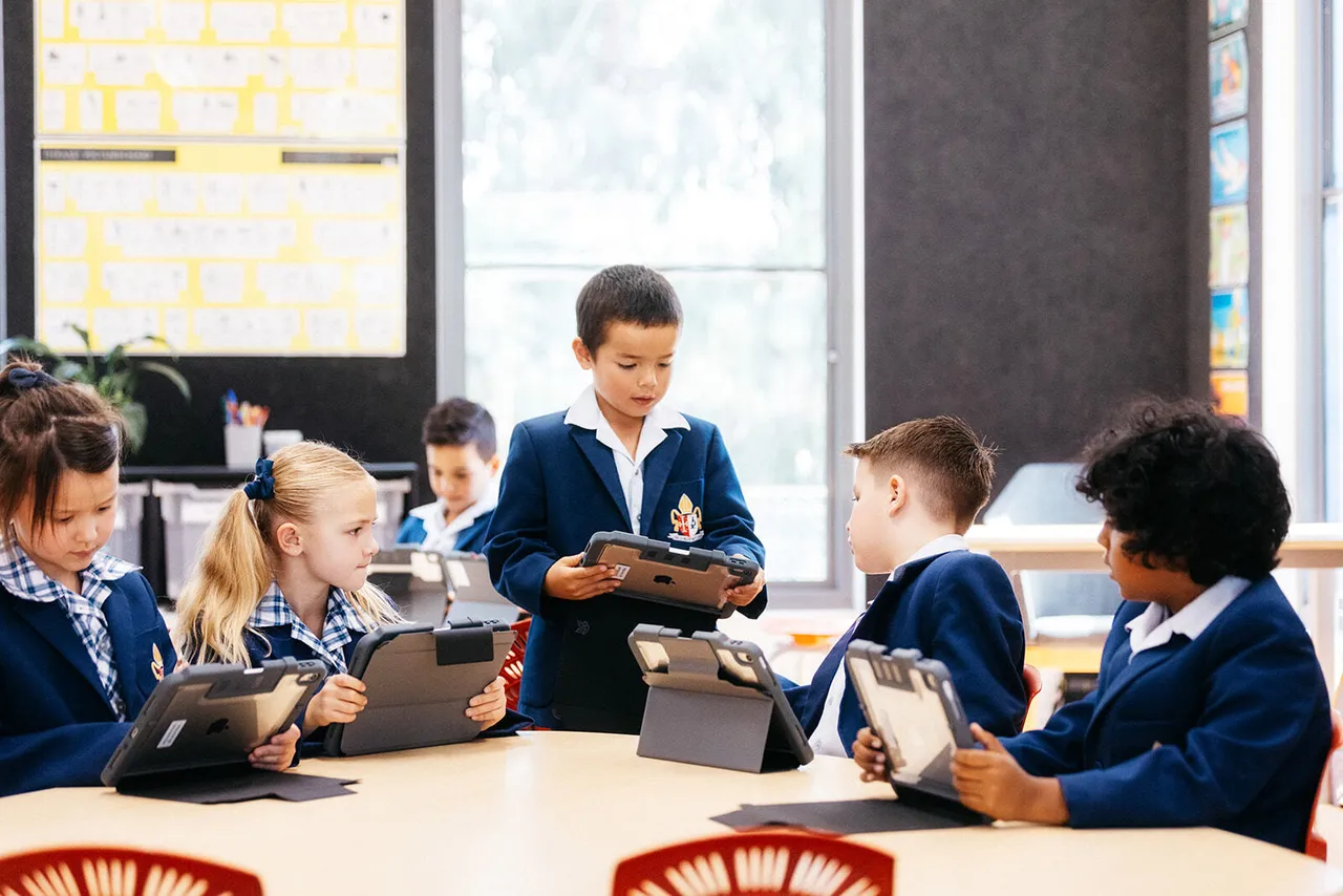 Group of primary school aged students engaged in a discussion while learning on iPads inside the Prep to Year 2 building at Canowindra Campus.