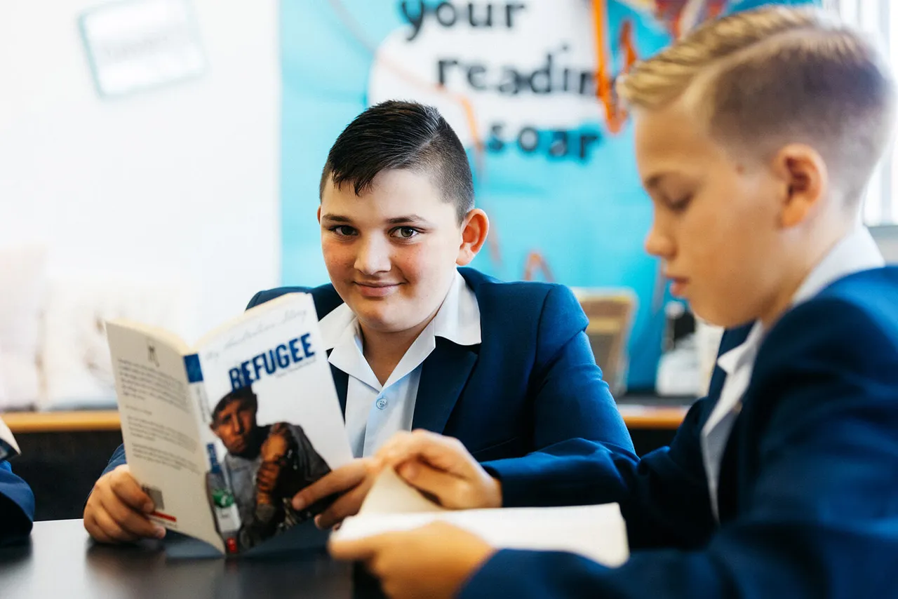 Upper primary school aged boy holding a book and looking at the camera in the Middle School library at Yirramboi Campus