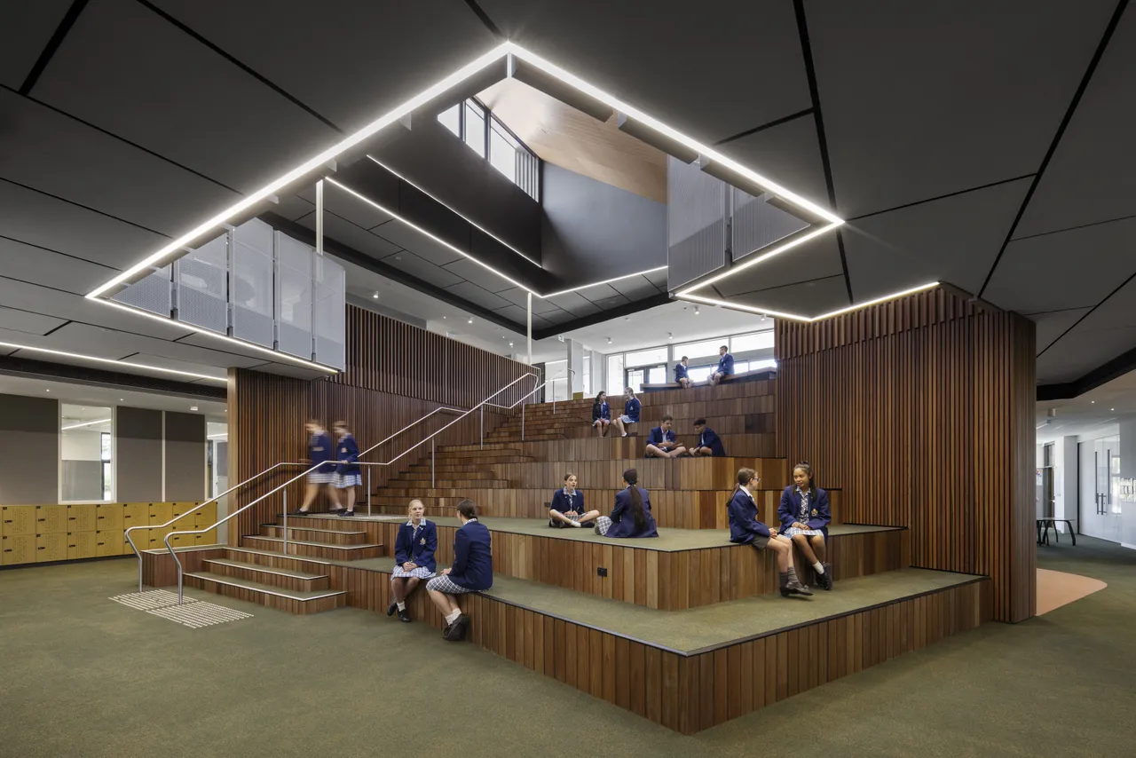 A collection of lower primary school aged students sitting on the steps of a large internal amphitheatre in Overnewton's award winning 6/7 Learning Centre located at Yirramboi Campus, Keilor.