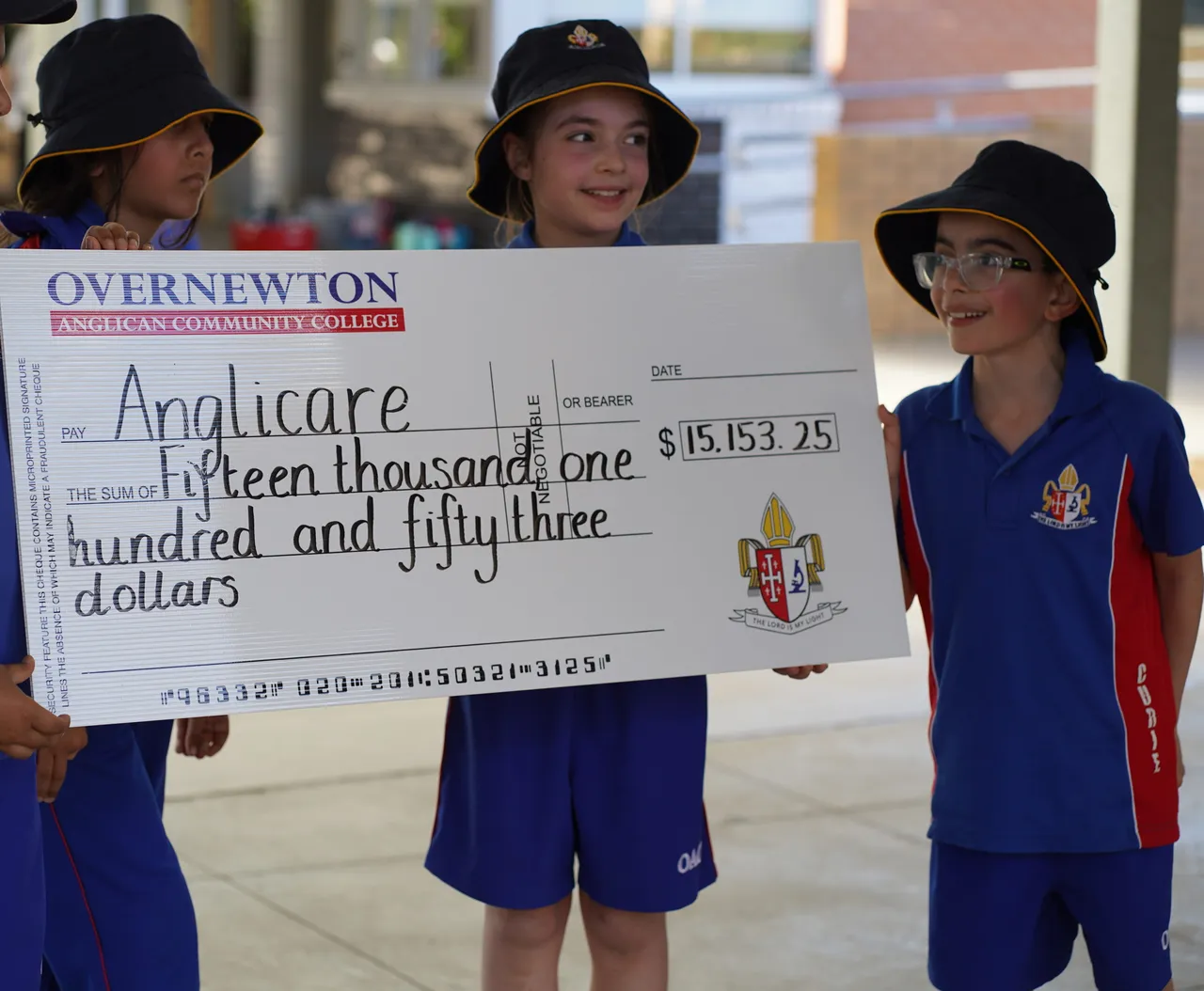 Four primary school aged students holding a large donation cheque for Anglicare Australia, representing Overnewton’s community giving efforts.
