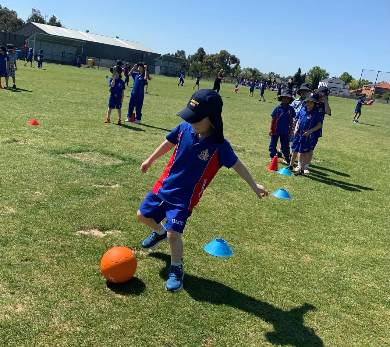 Lower primary school aged students developing gross motor skills by kicking balls through obstacles during a House Activate Day, part of Overnewton’s extensive co-curricular program.