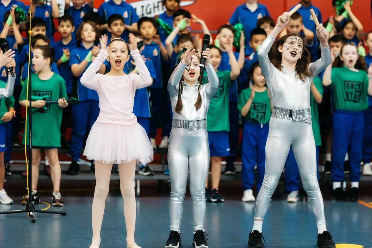 Primary school aged students performing with peers as part of Pasteur House (green) during Overnewton’s Encore House performance, with three costumed students front and centre leading the group with flair and confidence.