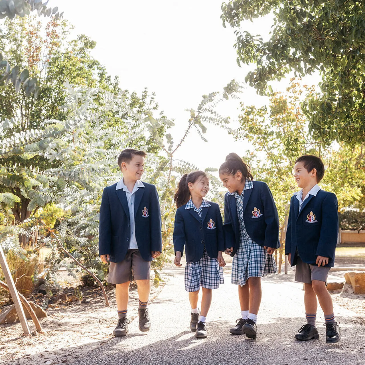 Four Junior School students walking together along the tree-lined nature footpath at Canowindra Campus, enjoying the natural surroundings on their way through the grounds.
