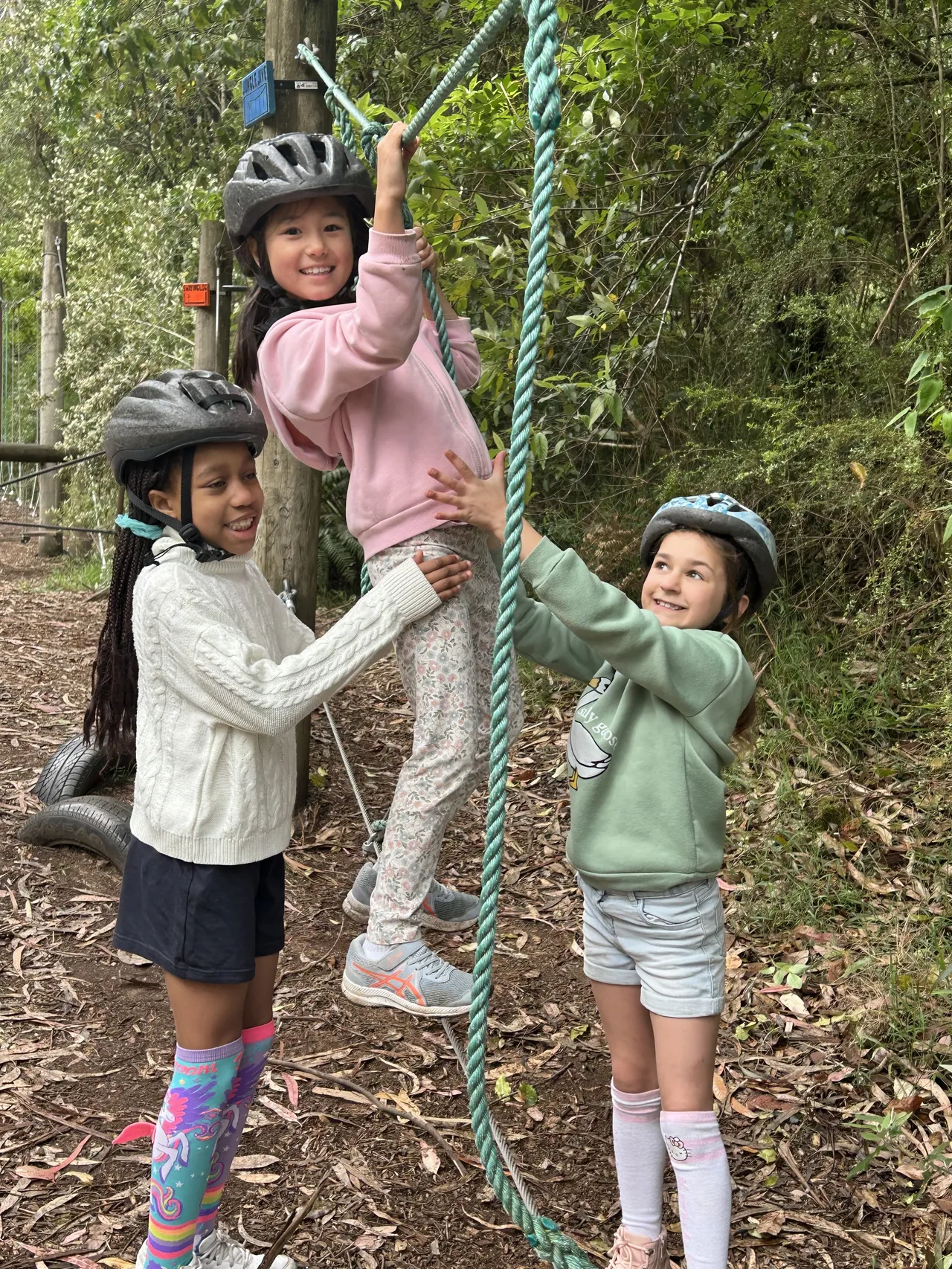 Three lower primary school aged students navigating a ropes course during the Year 2 Outdoor Adventure Camp—an experience designed to foster friendships, build resilience, and strengthen teamwork as part of the Overnewton Camps program.