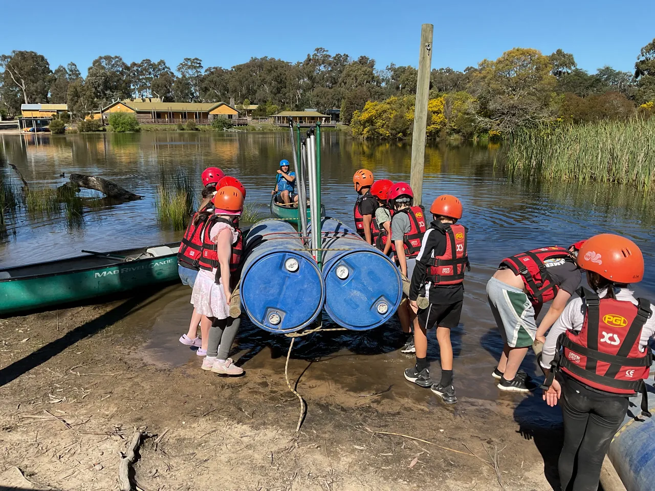 A group of lower primary school aged students lifting a team-built water raft into a small lake at the Year 3 Outdoor Adventure Camp—an engaging experience designed to foster friendships, build resilience, and strengthen teamwork as part of the Overnewton Camps program.