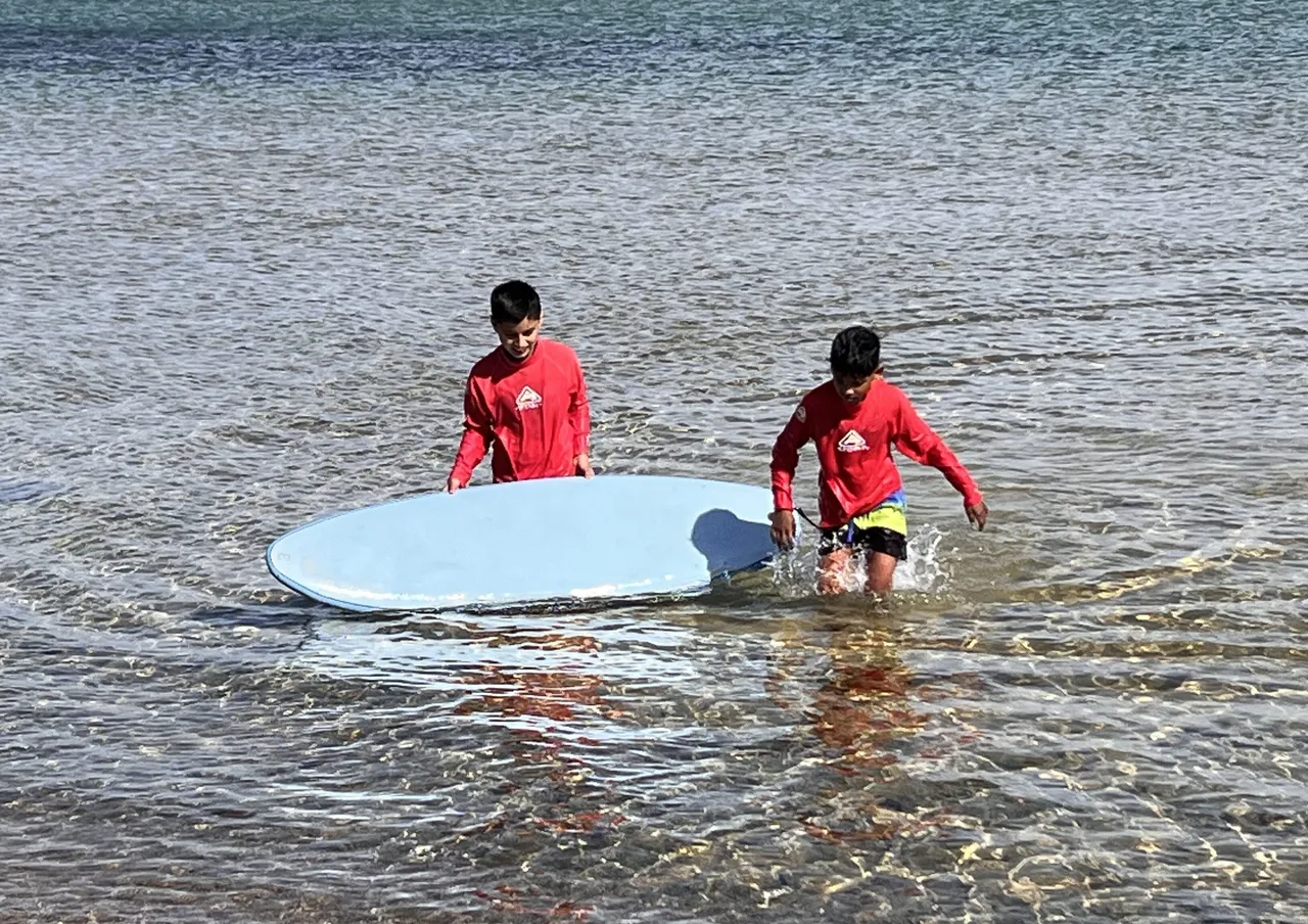 Two primary school aged students on Year 4 camp, enjoying the outdoor experience while paddle boarding together on the water.