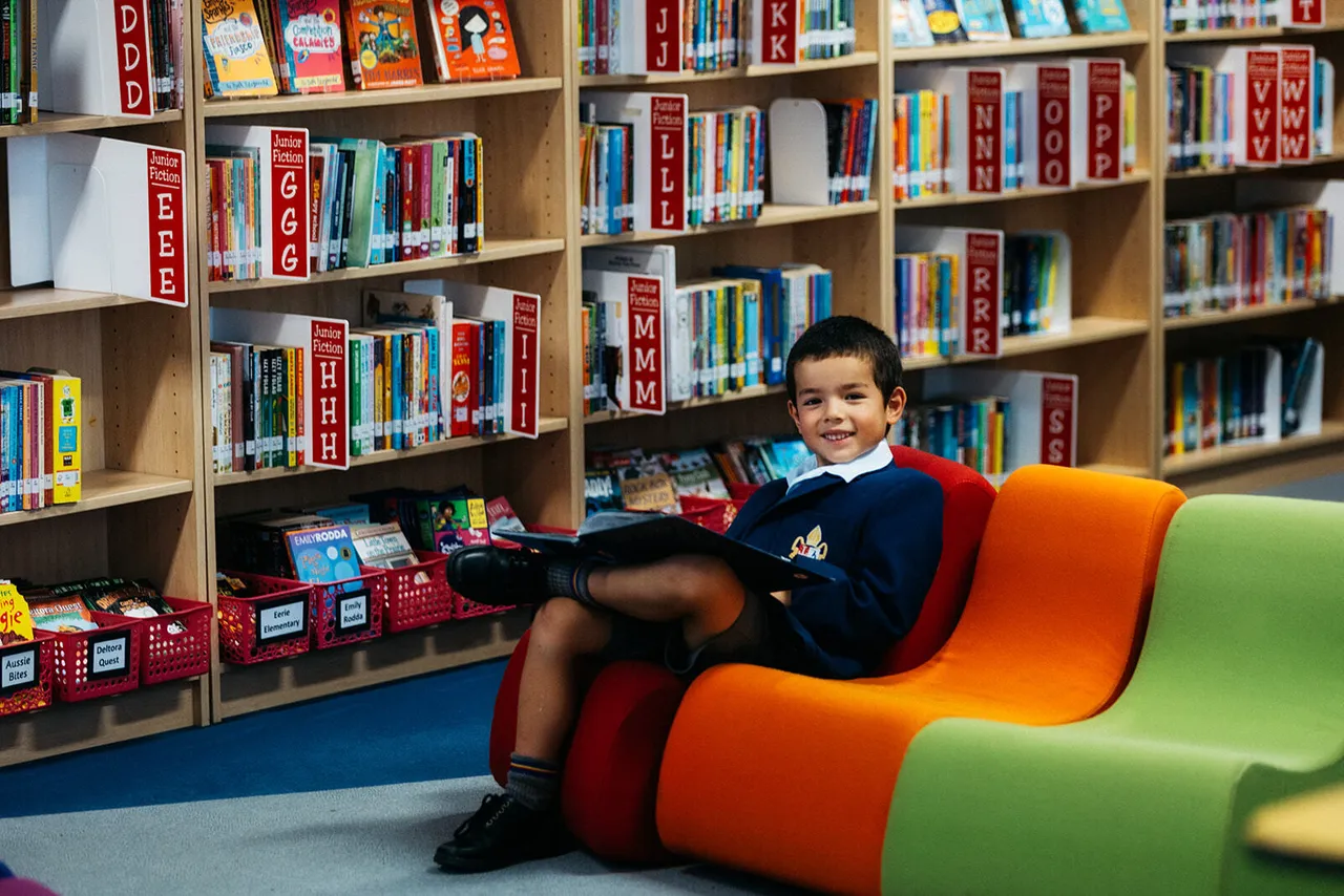 Lower primary school aged boy reading a book in the colourful Junior School library at Canowindra Campus.