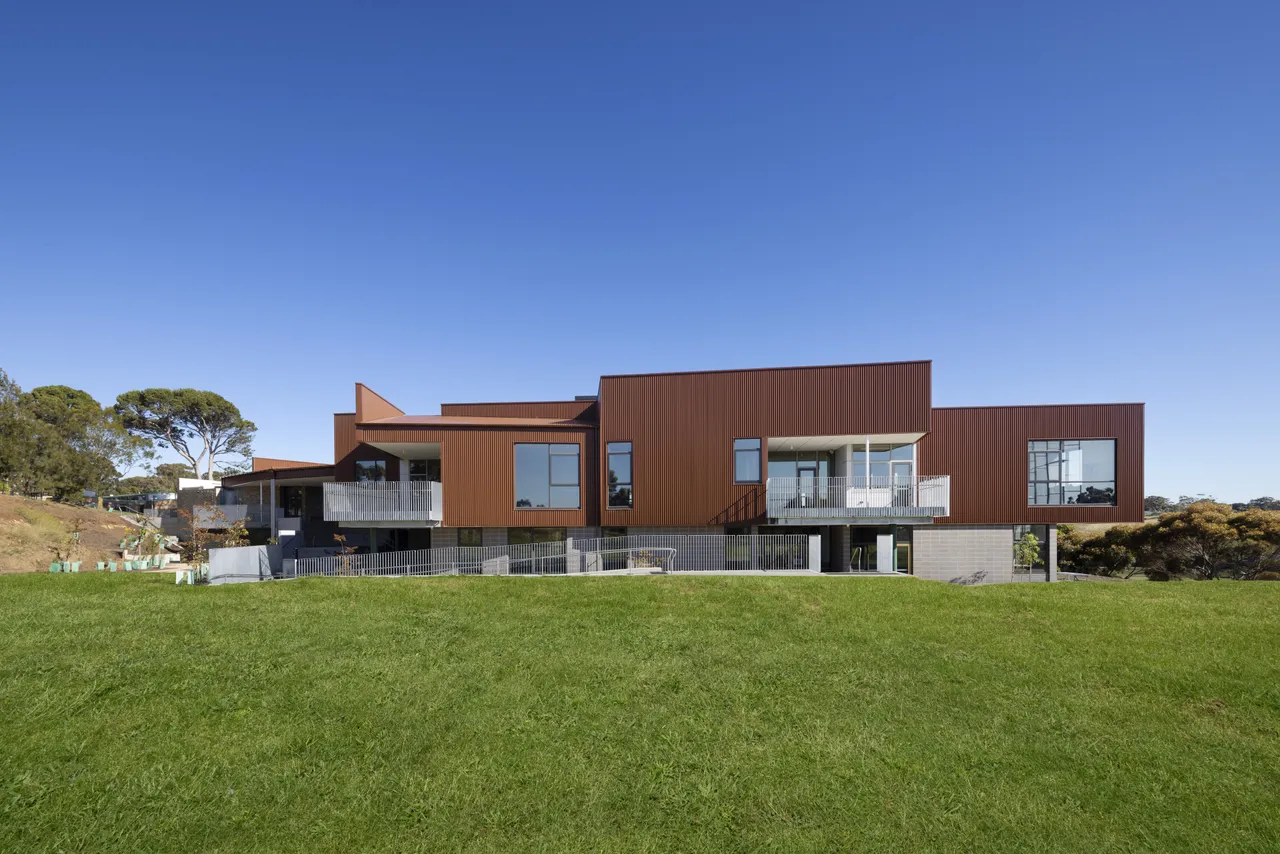 External view of the award-winning Middle School building at Yirramboi Campus, showcasing its striking architectural angles and balcony, set against a bright blue sky with green grass in the foreground.