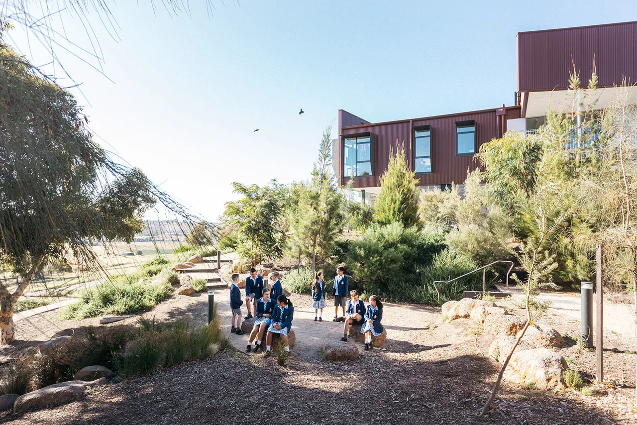 A large group of upper primary and lower high school aged students enjoying the outdoors among trees and natural greenery, with the award-winning Middle School building at Yirramboi Campus in the background.
