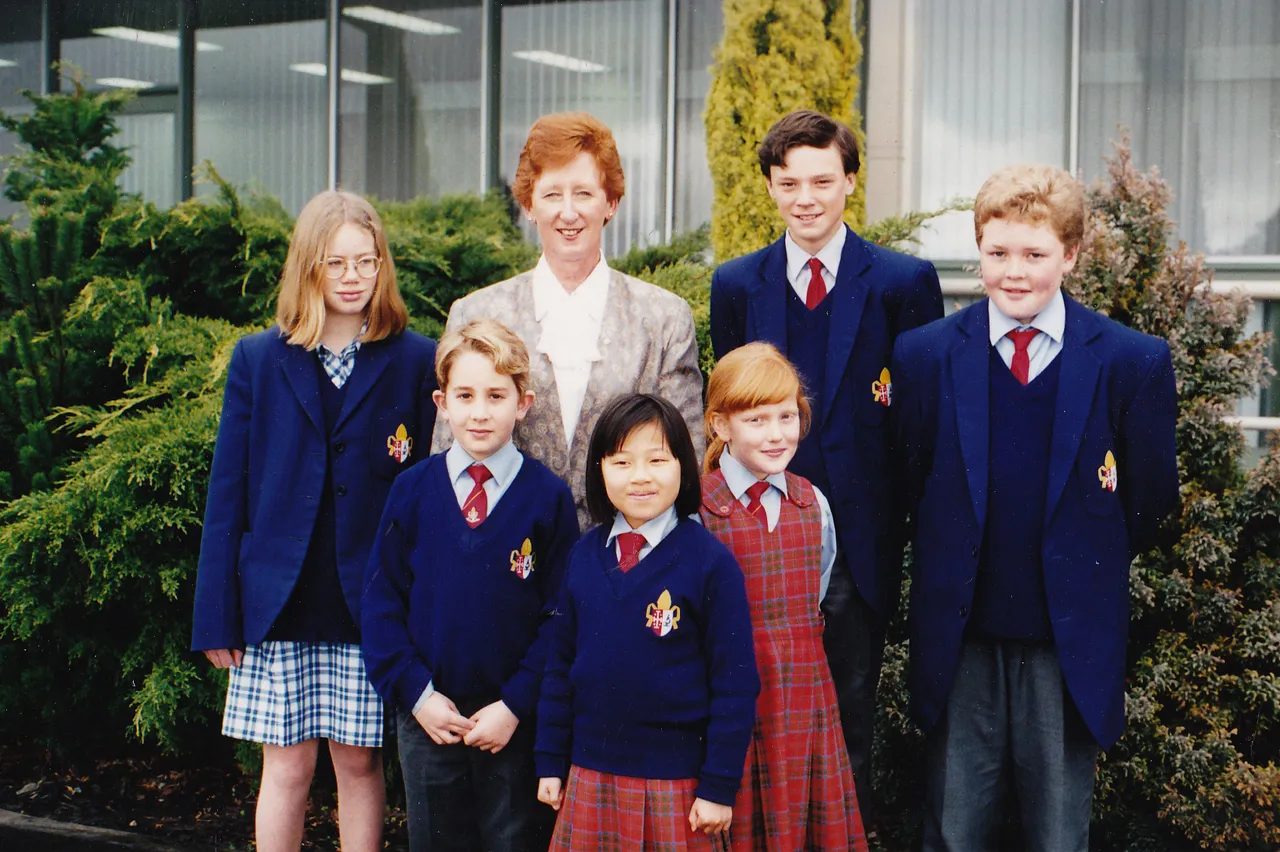 Archival photo from 1996 of the Principal standing with a group of students in front of her office at Overnewton, capturing a moment of school life and leadership during that time.