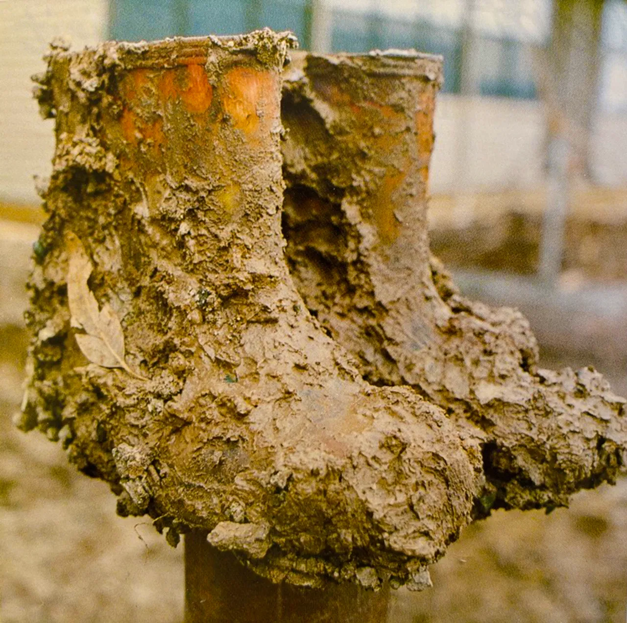 Archival photo of a pair of orange gumboots covered in mud, sitting on a post as a symbolic reminder of the early days of Overnewton when the grounds were still being established.