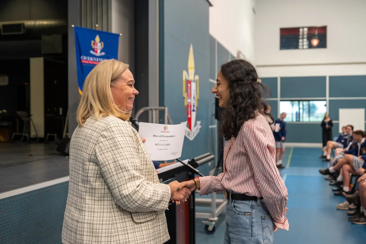Principal proudly presenting an academic achievement certificate to a student during an assembly at Overnewton, recognising outstanding student success.