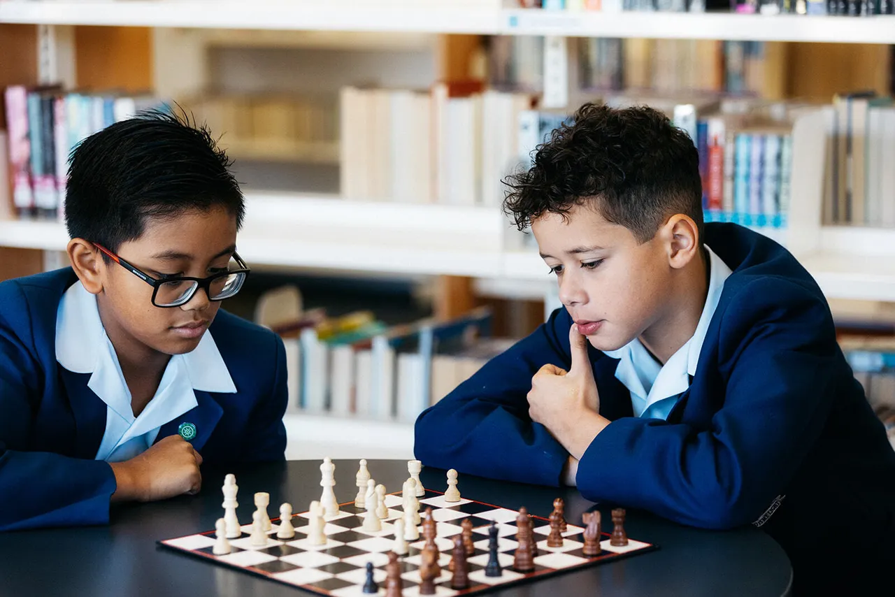 Two upper primary school aged students in the Middle School library at Yirramboi Campus, deep in thought while playing a game of chess together.