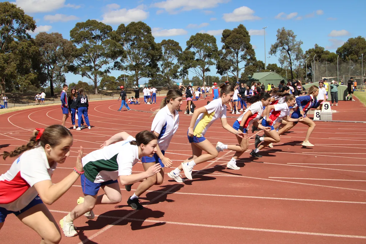 A large group of upper secondary school aged students captured mid-stride as they launch off their marks to compete in a track event at the Senior School House Athletics Carnival.