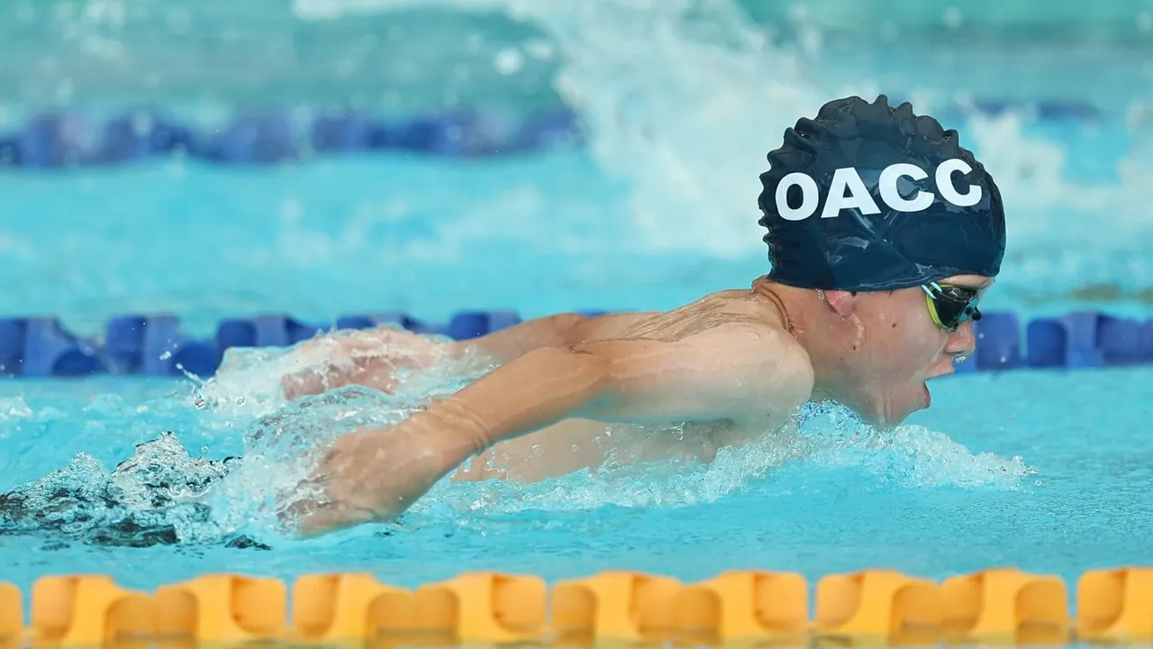 Middle School student mid-stroke while competing in a swimming race, wearing goggles and an Overnewton-branded swimming cap in the pool.