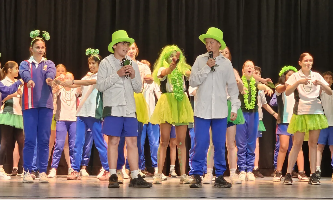 A large group of middle secondary school aged students performing in vibrant green-themed costumes, proudly representing Pasteur House in the annual Middle School Battle of the Houses—an Encore Performing Arts Co Curricular event