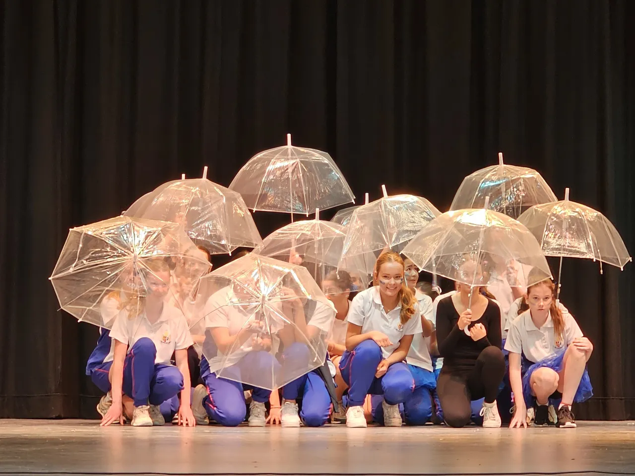 A group of middle secondary school aged students performing under a cluster of clear umbrellas on stage, as part of the Middle School Battle of the Houses—a creative and spirited showcase within Overnewton’s Encore Performing Arts Co Curricular program