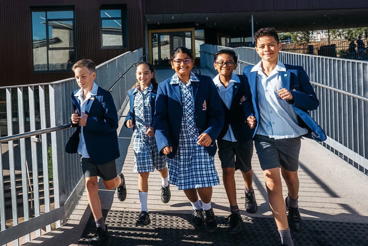 A group of happy upper primary and lower secondary aged students photographed running towards the camera across the bridge that adjoins the Year 6 and 7 building and the Year 5 & 8 buildings at Middle School, Yirramboi Campus Keilor.