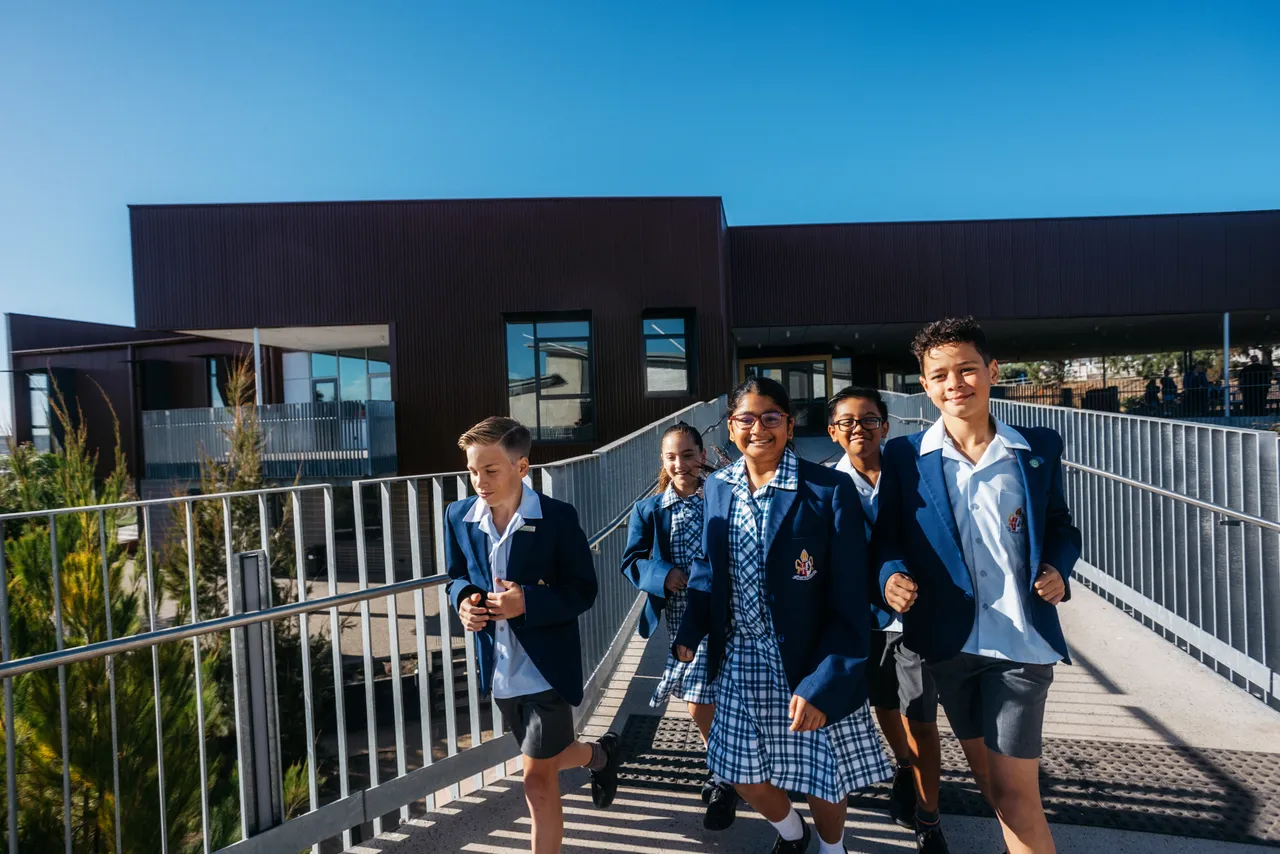 Middle School students running across the bridge from the award-winning Middle School building at Yirramboi Campus, with the building and a bright blue sky visible in the background.