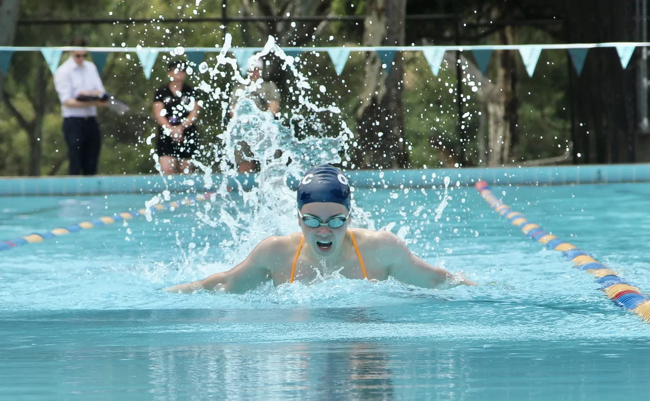 Low-angle shot at the waterline of a powerful senior secondary school aged swimmer mid-stroke during the Butterfly, coming up for air at the annual Activate Senior Swimming Carnival.