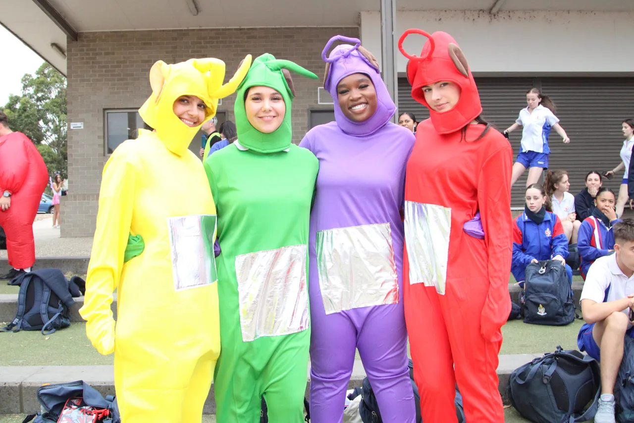 A group of four upper secondary school aged students smiling at the camera in bright Teletubbi's costumes at the Senior School House Athletics Carnival.