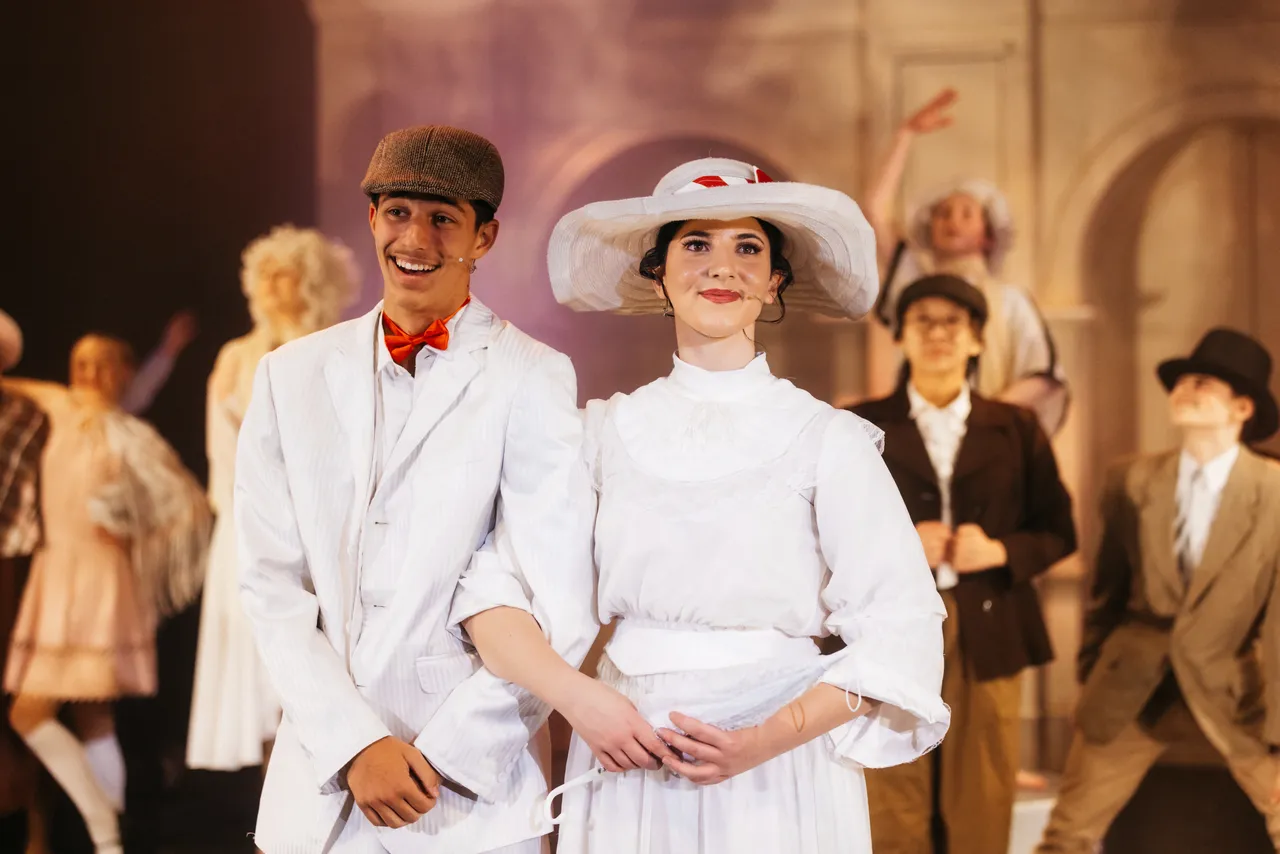 The two lead actors of the annual College Musical, Mary Poppins, gazing out over the audience with the supporting cast visible in the background.