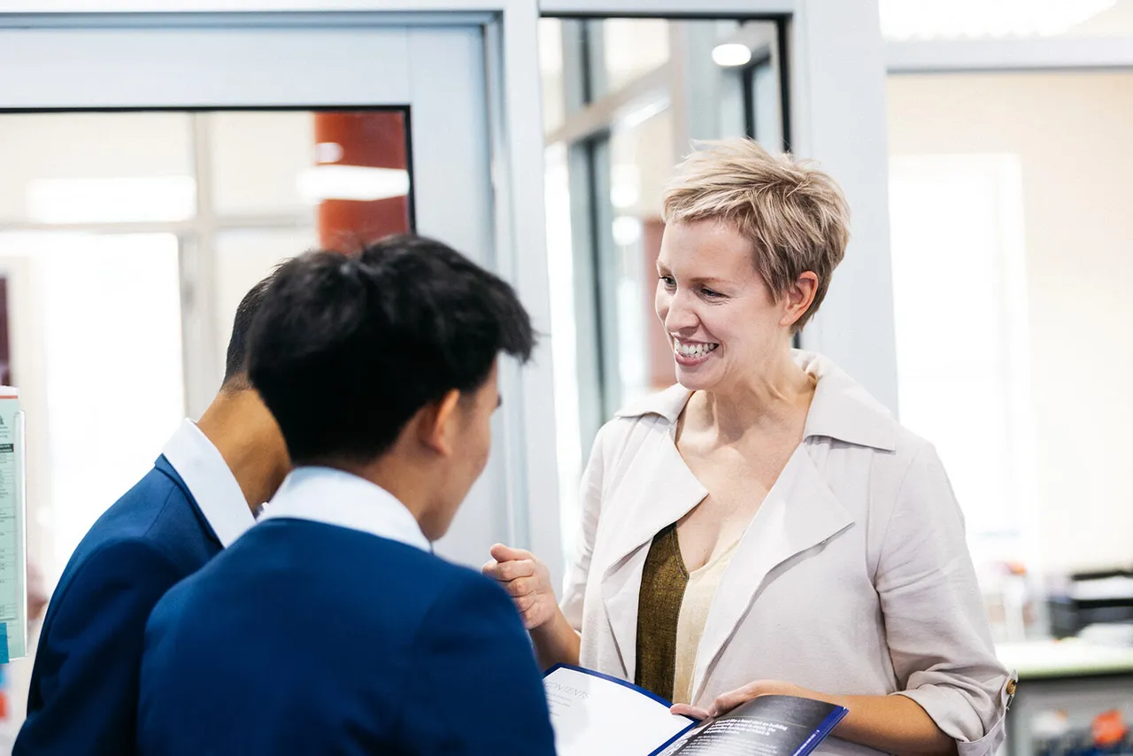 A visibly engaged careers practitioner animatedly discussing university options with two senior secondary school aged students at Overnewton’s Careers Centre, holding a university course brochure.