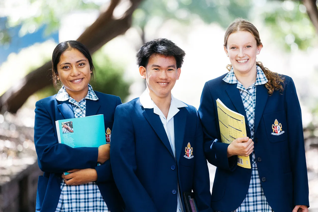 A small group of upper senior secondary school aged students in academic uniform smiling brightly at the camera, with two students holding exercise books.
